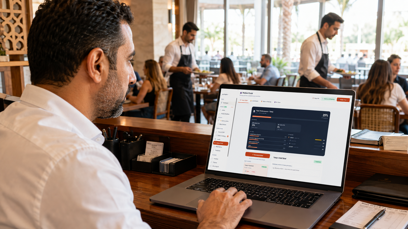 An owner reviews today's team performance and staff brief on the DineCore Waiters Portal, with the restaurant floor busy behind him